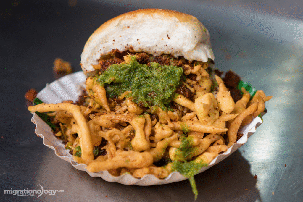 Spicy vada pav served with green chili and chutney on a street cart in Mumbai